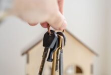 Mano sosteniendo llaves junto a una pequeña casa de madera, símbolo del alquiler de vivienda