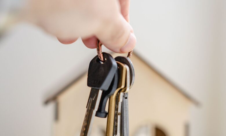 Mano sosteniendo llaves junto a una pequeña casa de madera, símbolo del alquiler de vivienda