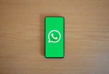 Celular sobre una mesa de madera con el logo de WhatsApp en pantalla