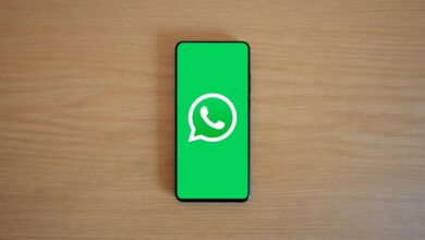 Celular sobre una mesa de madera con el logo de WhatsApp en pantalla