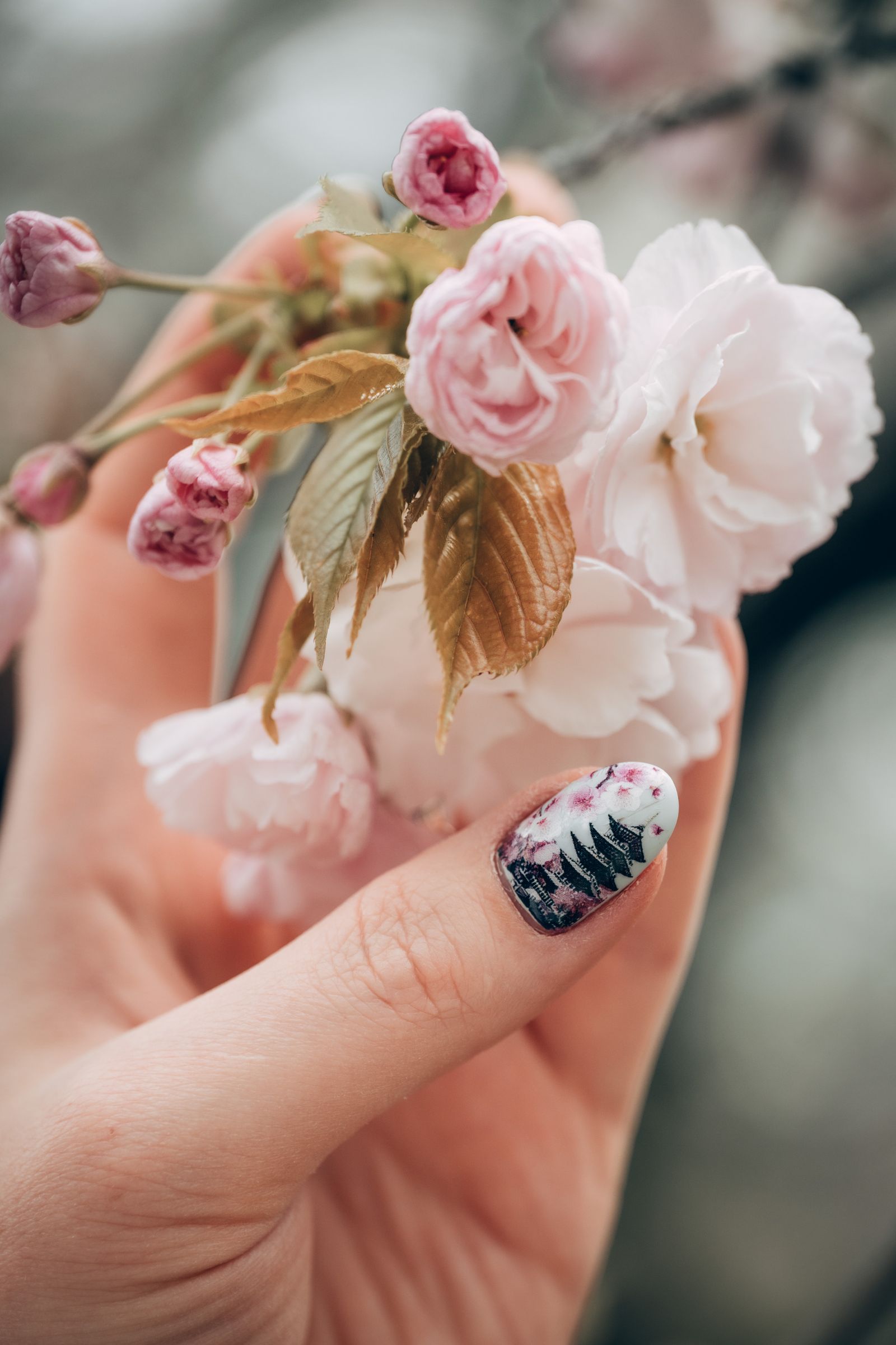 Mano que sostiene flores rosadas y muestra una uña con diseño floral