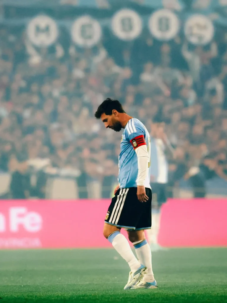Messi camina con la cabeza baja sobre el césped mientras la tribuna detrás lo aplaude.