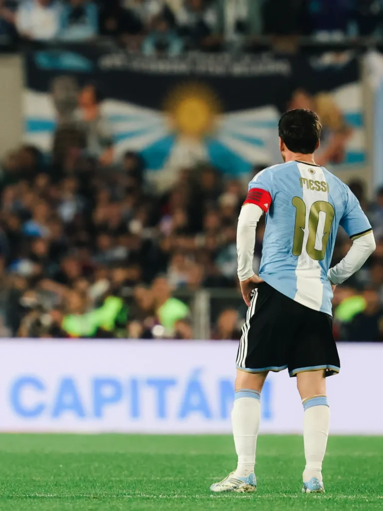 Messi de espaldas con las manos en la cintura, con la cinta de capitán, frente a un cartel que dice "Capitán".