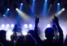 Público con las manos en alto frente a un escenario iluminado en un recital