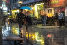 Personas con paraguas en una calle de noche vista a través de un vidrio mojado por la lluvia