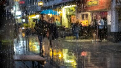 Personas con paraguas en una calle de noche vista a través de un vidrio mojado por la lluvia