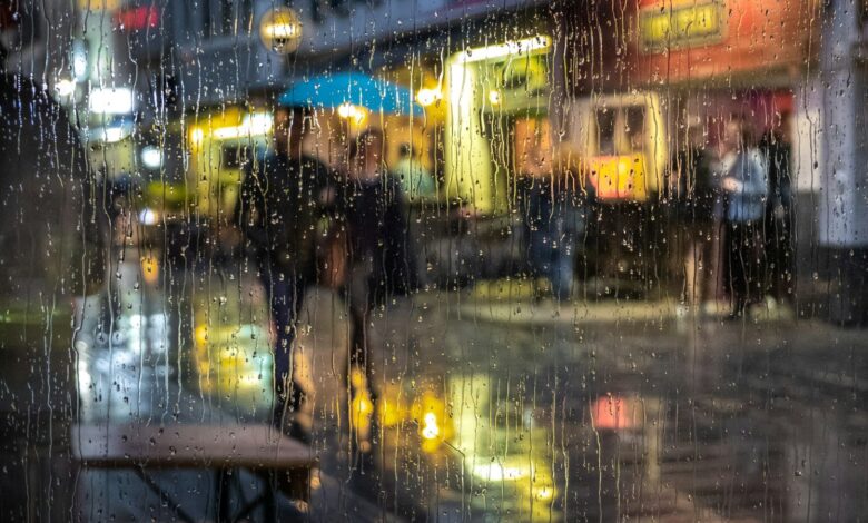 Personas con paraguas en una calle de noche vista a través de un vidrio mojado por la lluvia
