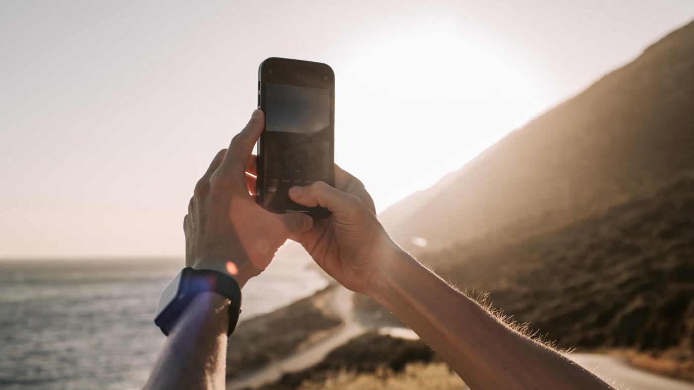 Persona fotografiando el atardecer sobre la costa con el celular