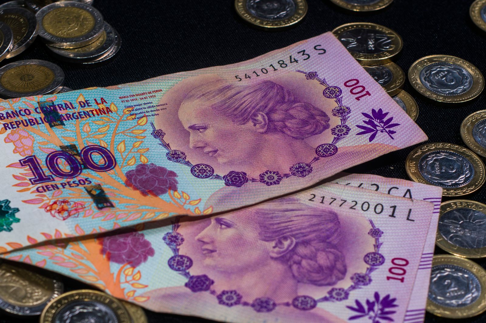 Billetes de cien pesos argentinos y monedas sobre una mesa
