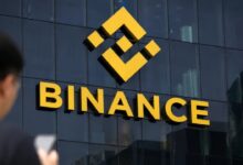 Fachada de un edificio con el logo de Binance y una persona mirando el celular