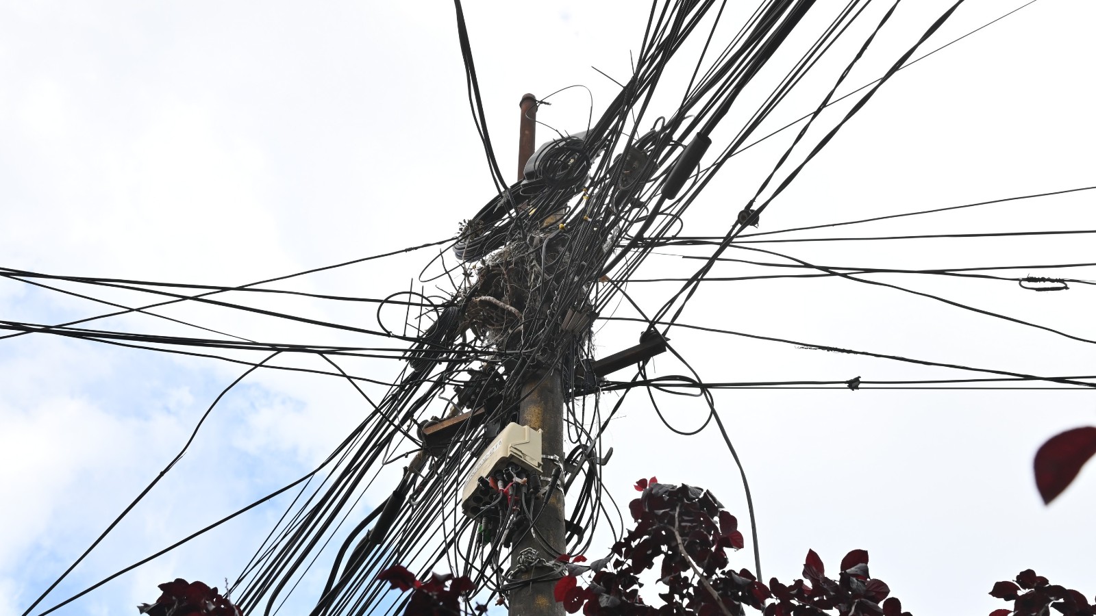 Poste con una maraña de cables aéreos en una calle de Rosario