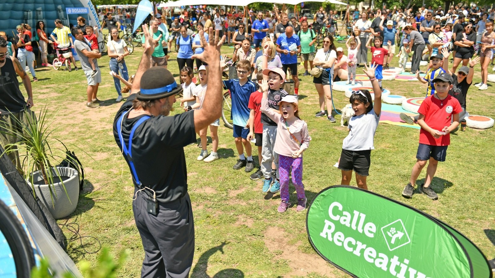 Chicos y familias hacen actividad física junto a un cartel de Calle Recreativa en un parque de Rosario