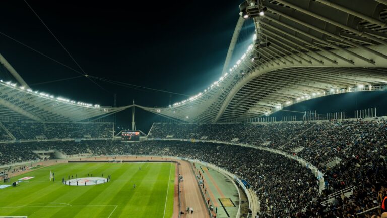 Estadio de fútbol iluminado de noche con la tribuna llena