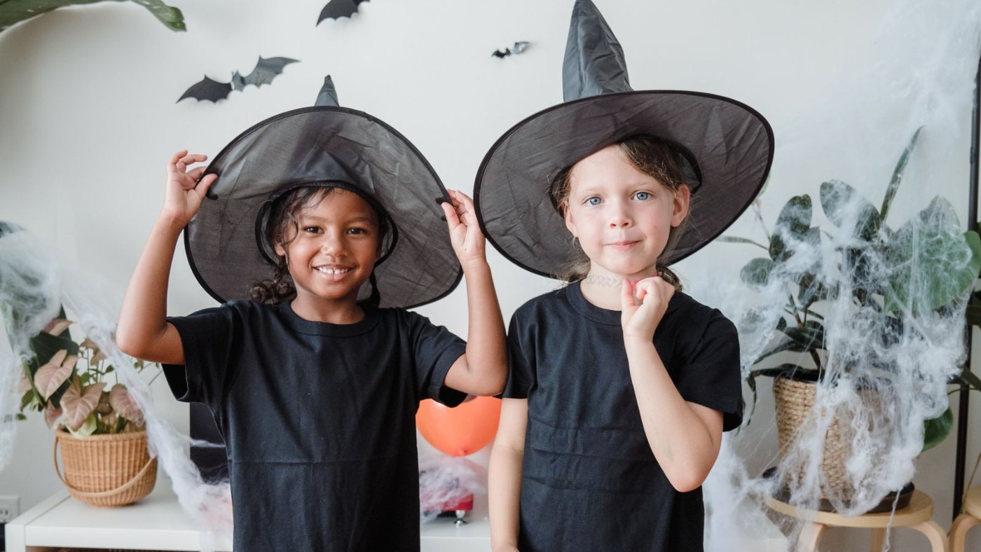 Dos chicos con sombreros de bruja en una pared decorada con murciélagos
