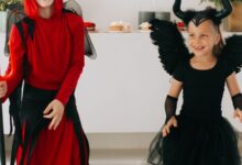 Dos chicos disfrazados de diablo y ángel oscuro riendo en una fiesta de Halloween