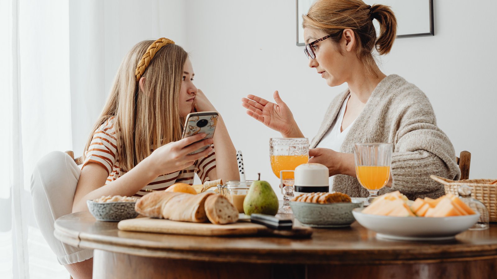 Madre y adolescente conversando en la mesa con un celular en la mano