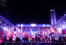 Escenario principal de la Fiesta de las Colectividades de noche, con el Monumento a la Bandera iluminado de fondo