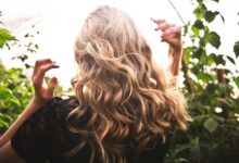 Mujer de espaldas con pelo largo ondulado rubio dorado con reflejos, entre plantas verdes
