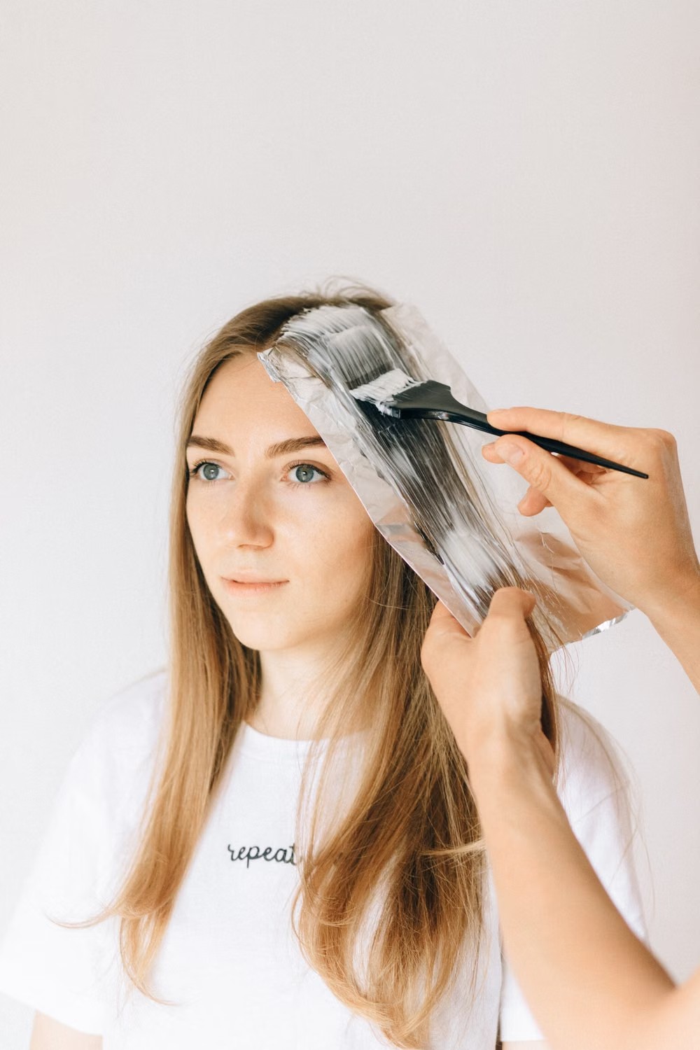 Colorista aplicando tintura con pincel sobre mechones de una clienta de pelo castaño claro