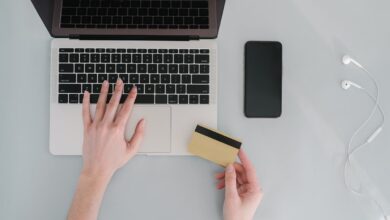 Manos sobre el teclado de una notebook con una tarjeta bancaria al lado del celular