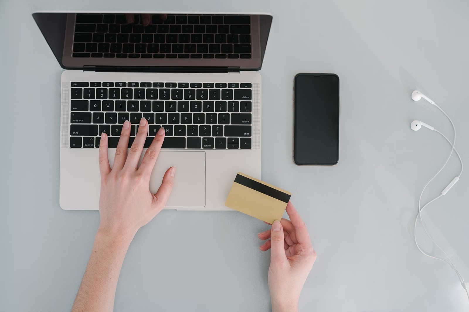Manos sobre el teclado de una notebook con una tarjeta bancaria al lado del celular
