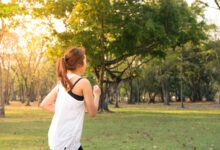 Mujer trotando por un parque arbolado temprano por la mañana
