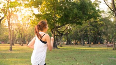 Mujer trotando por un parque arbolado temprano por la mañana