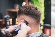 Barbero hace un degradado con máquina a un cliente joven en una barbería