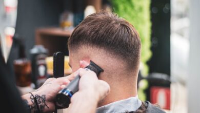 Barbero hace un degradado con máquina a un cliente joven en una barbería