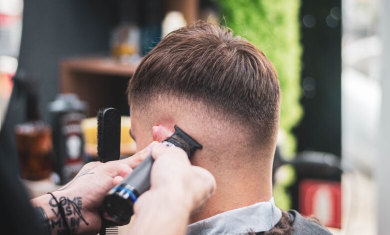 Barbero hace un degradado con máquina a un cliente joven en una barbería