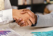 Dos personas dándose la mano sobre una mesa con documentos