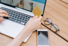Persona con una tarjeta en la mano mientras compra en una notebook