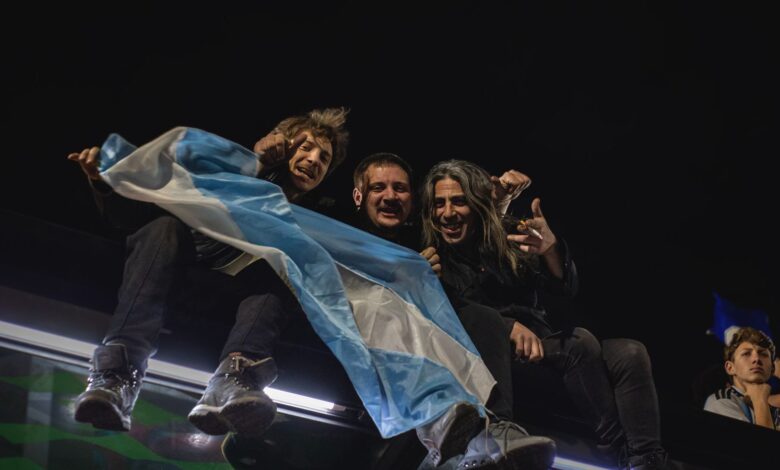 Hinchas argentinos con una bandera celeste y blanca de noche, celebrando un partido de la Selección