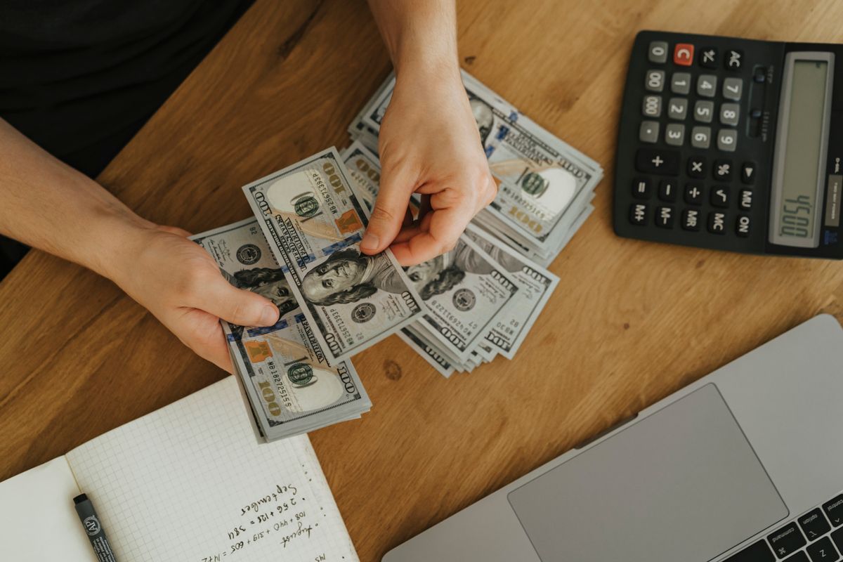 Manos contando billetes junto a una calculadora y un cuaderno
