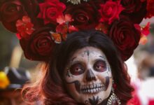 Mujer con maquillaje de Catrina y una corona de flores rojas, típica del Día de Muertos