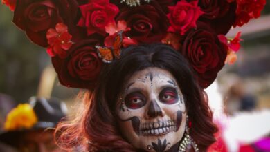 Mujer con maquillaje de Catrina y una corona de flores rojas, típica del Día de Muertos