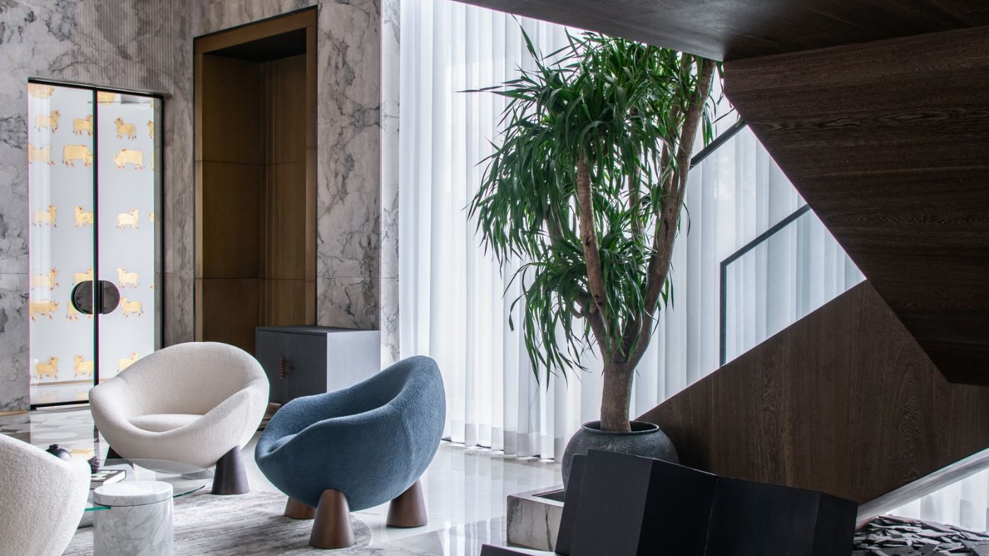 Interior de diseño con escalera, sillones y vegetación bajo un gran ventanal