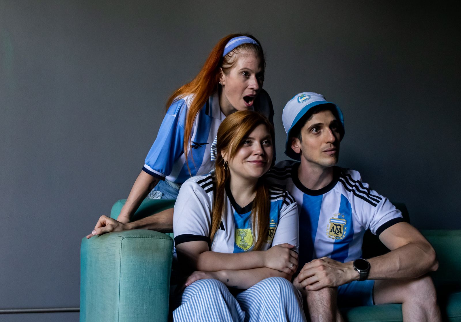 Tres hinchas con camisetas de la Selección argentina miran un partido con emoción