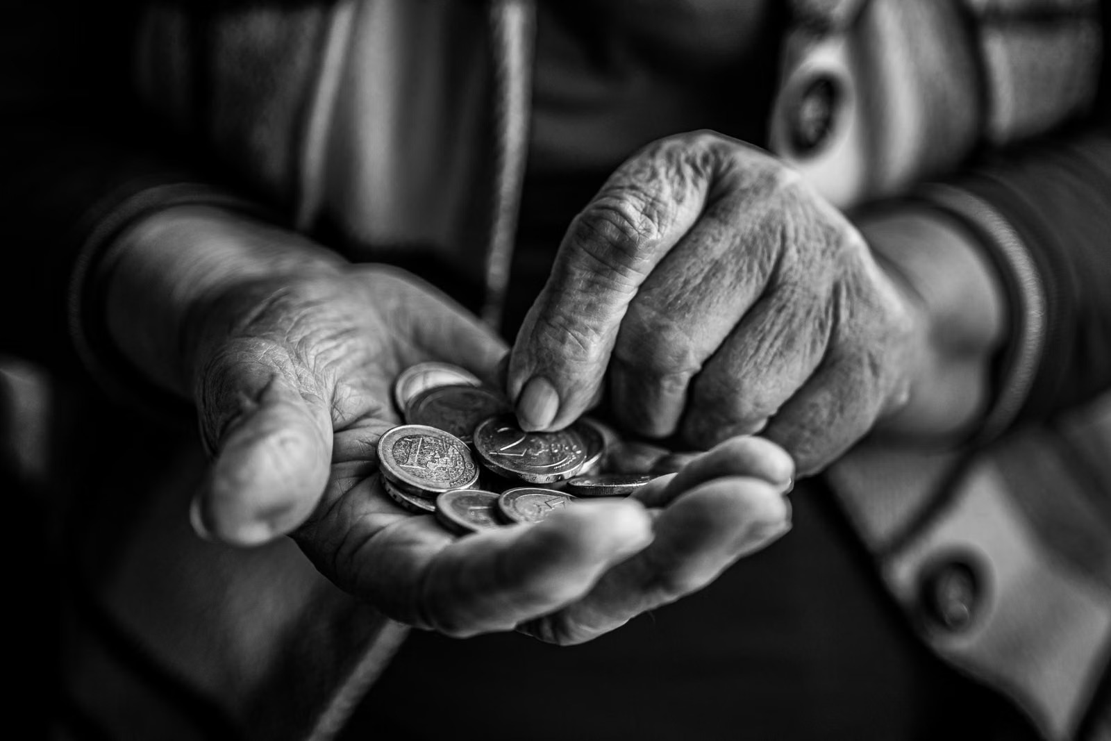 Manos de una persona mayor contando monedas en blanco y negro