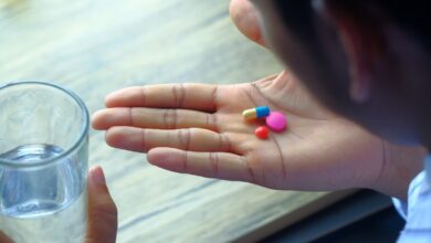 Mano con pastillas de colores y un vaso de agua, a punto de tomar la medicación
