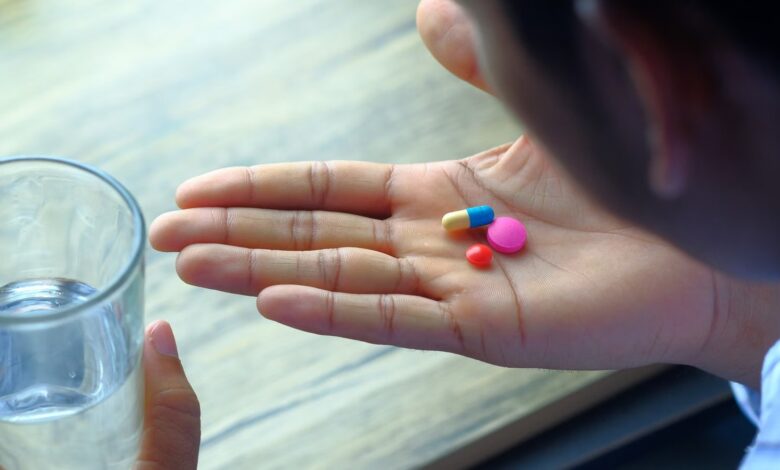 Mano con pastillas de colores y un vaso de agua, a punto de tomar la medicación