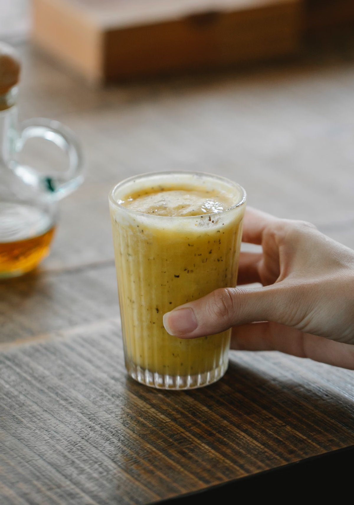 Mano sosteniendo un vaso de licuado amarillo de mango y naranja