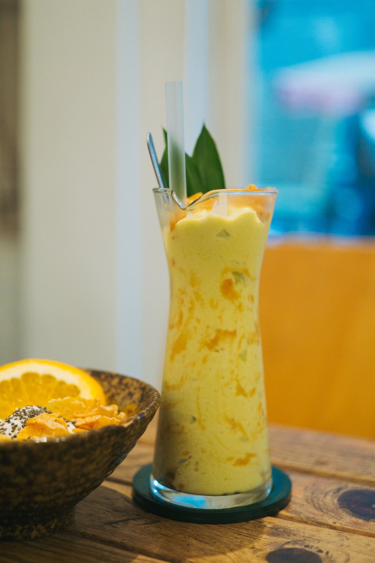 Licuado amarillo de ananá en un vaso alto junto a una naranja cortada