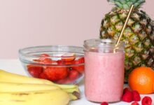 Licuado rosado de frutilla en un vaso junto a un ananá y frutillas frescas