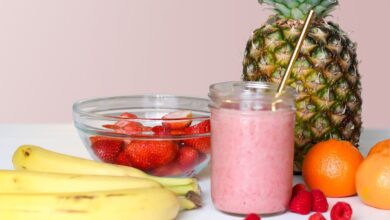 Licuado rosado de frutilla en un vaso junto a un ananá y frutillas frescas