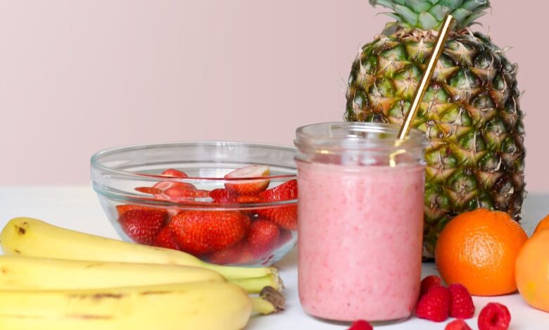 Licuado rosado de frutilla en un vaso junto a un ananá y frutillas frescas
