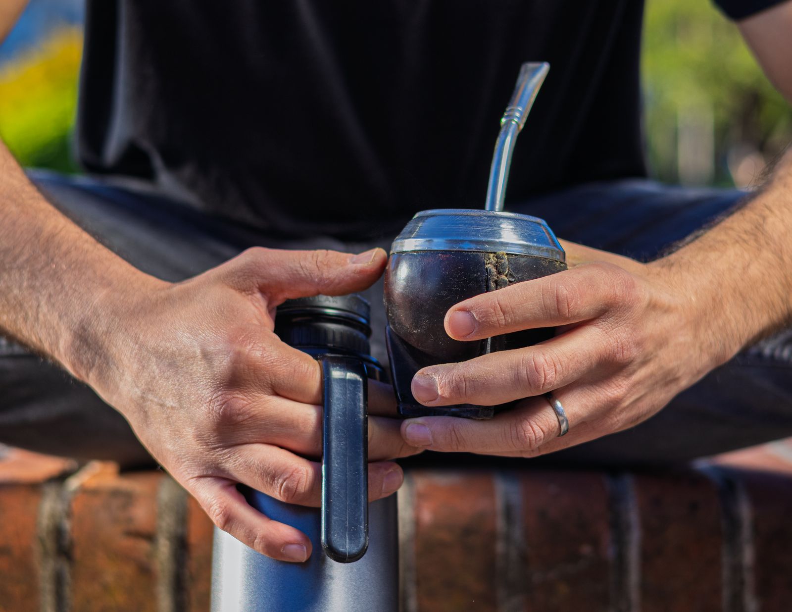 Manos sosteniendo un mate con bombilla y un termo al aire libre