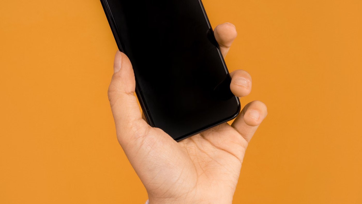 Mano sosteniendo un celular sobre un fondo naranja