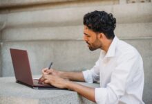 Hombre escribiendo en un cuaderno frente a su notebook