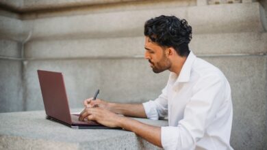 Hombre escribiendo en un cuaderno frente a su notebook